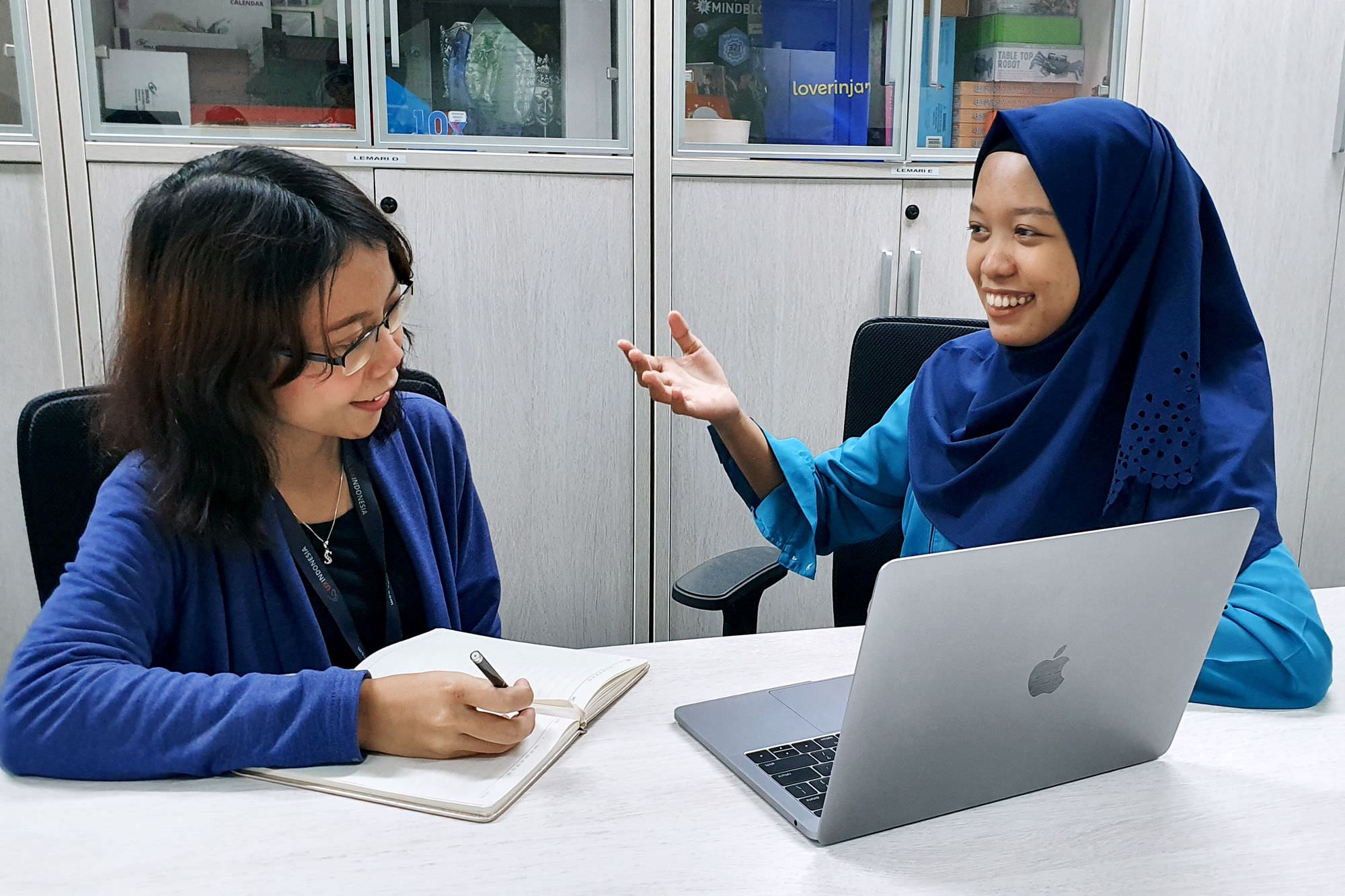 Two women participating in user interview. Researcher making notes as interviewee animatedly talks about their experience.
