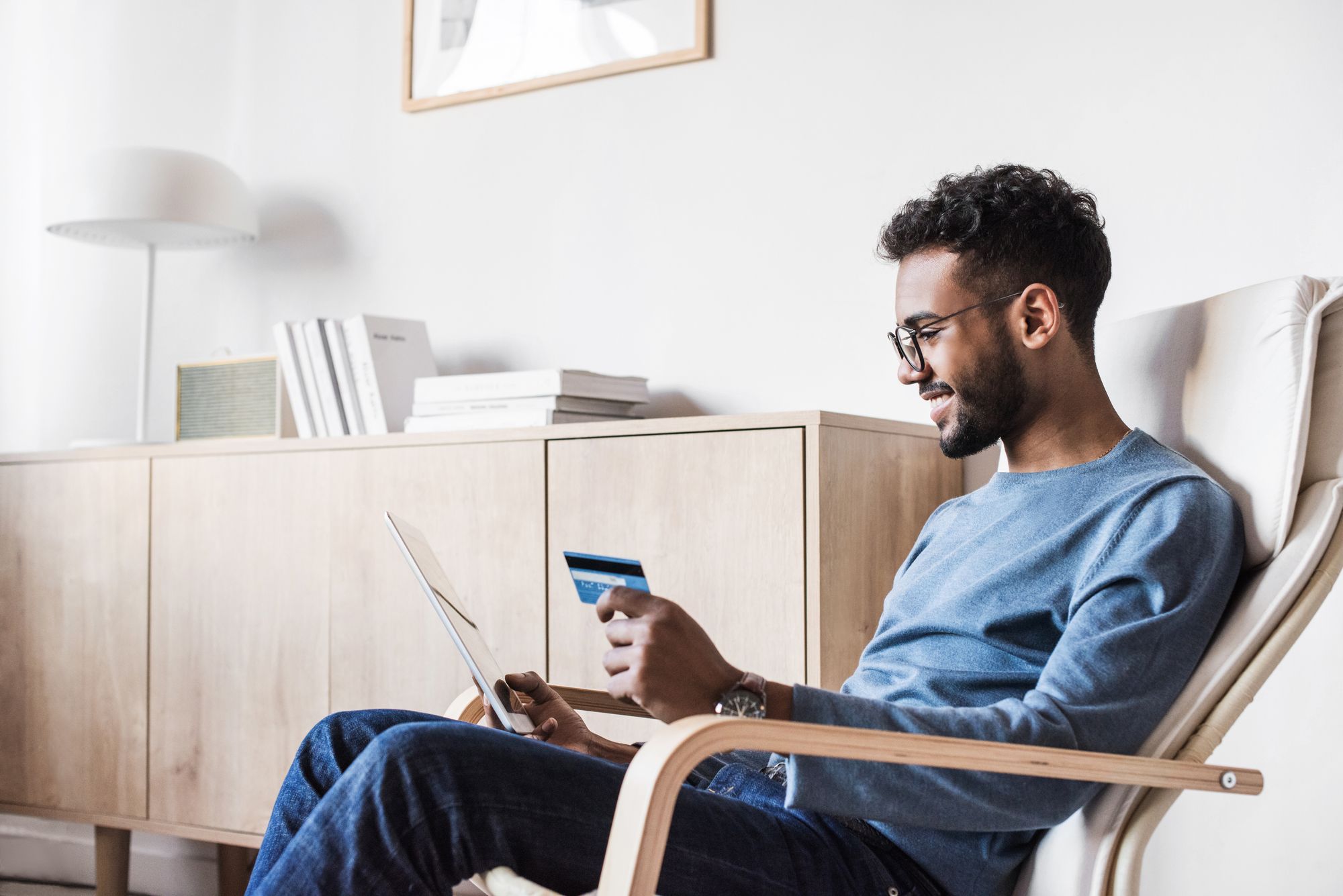 A person sitting on a reclining chair holding a credit card and a tablet.  