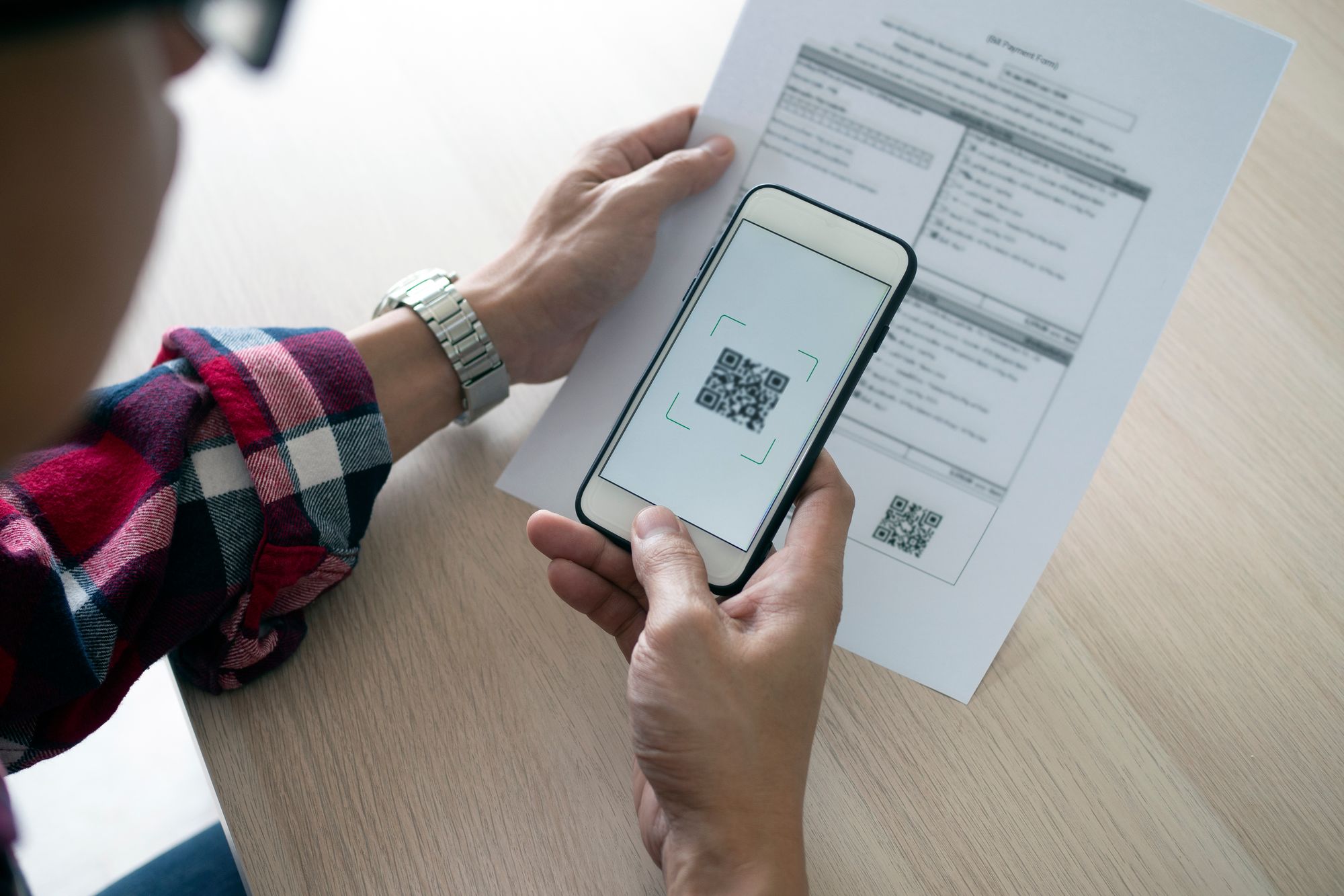 A person using their smartphone to scan a barcode on a paper document. 