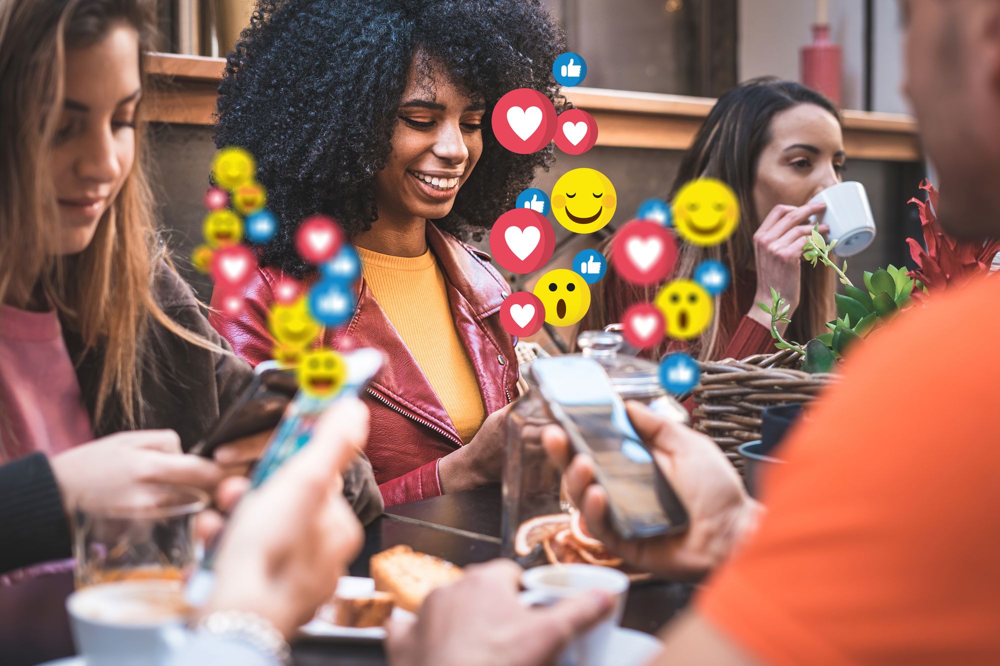 A group of people texting while having lunch on the patio with emojis emerging from their phones.