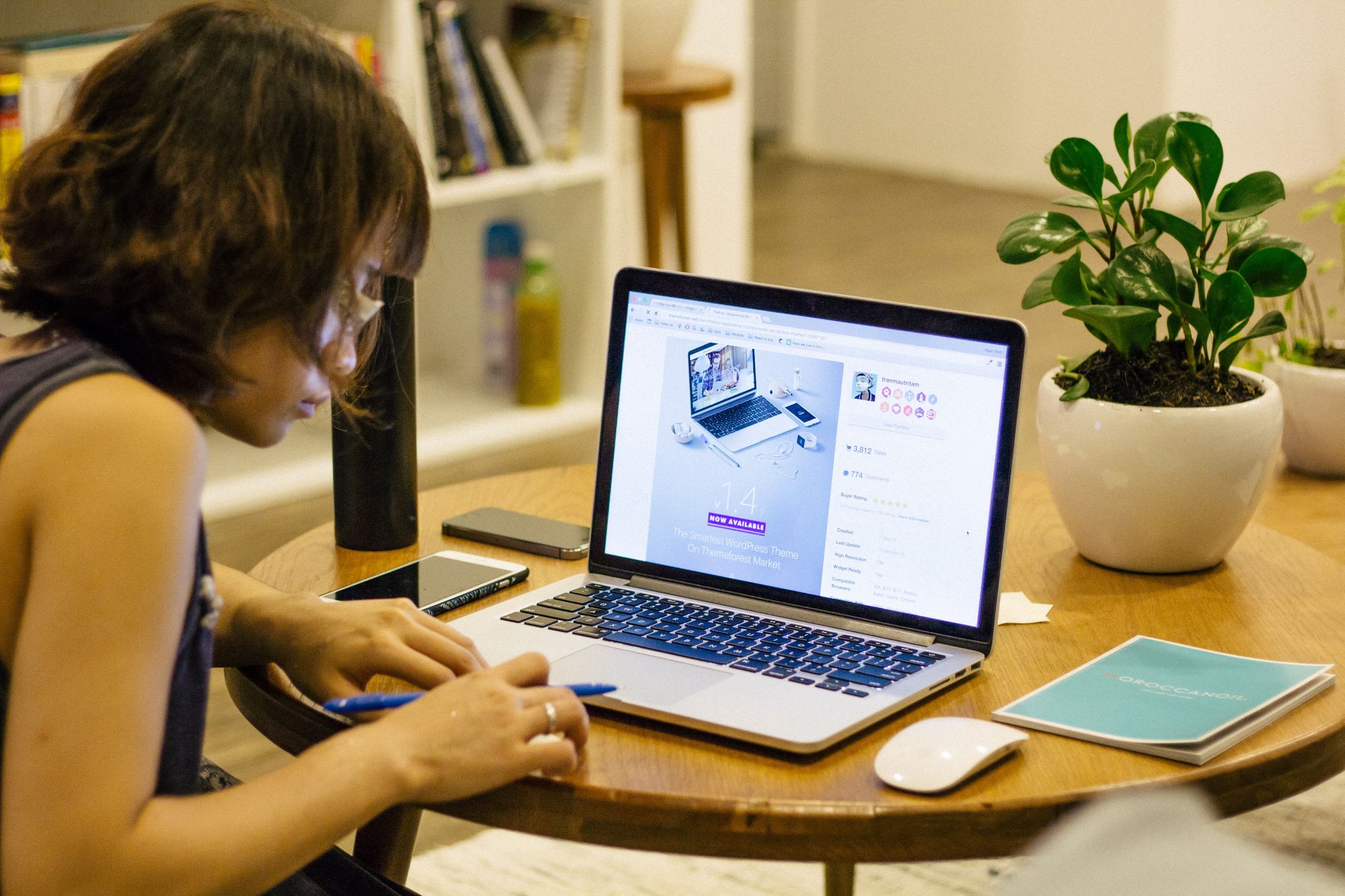 A person taking notes on a coffee table and browsing on a laptop computer.