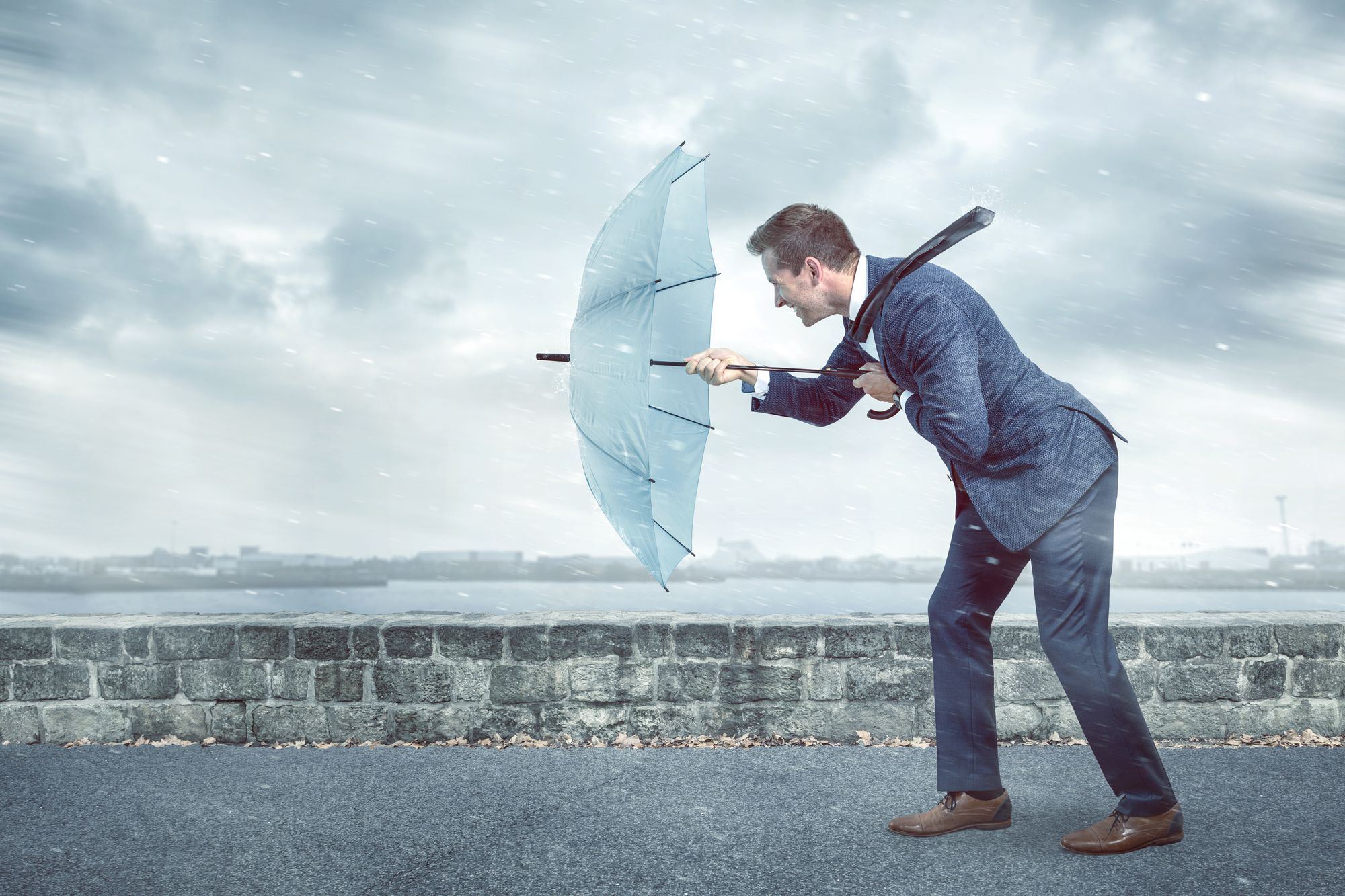 Une personne vêtue d’un complet bleu tenant un parapluie tendu devant elle pour se protéger d’un vent fort. 