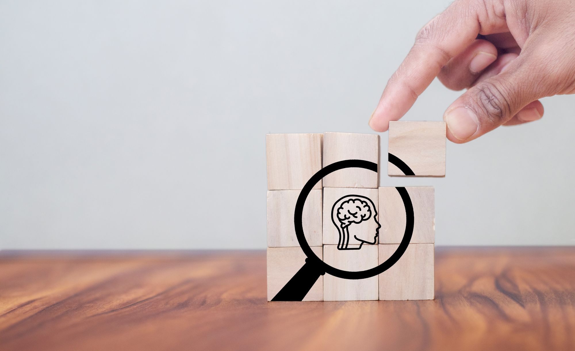 A hand places the last cube in a wooden puzzle to complete the image of a magnifying glass  focusing on a person's brain.