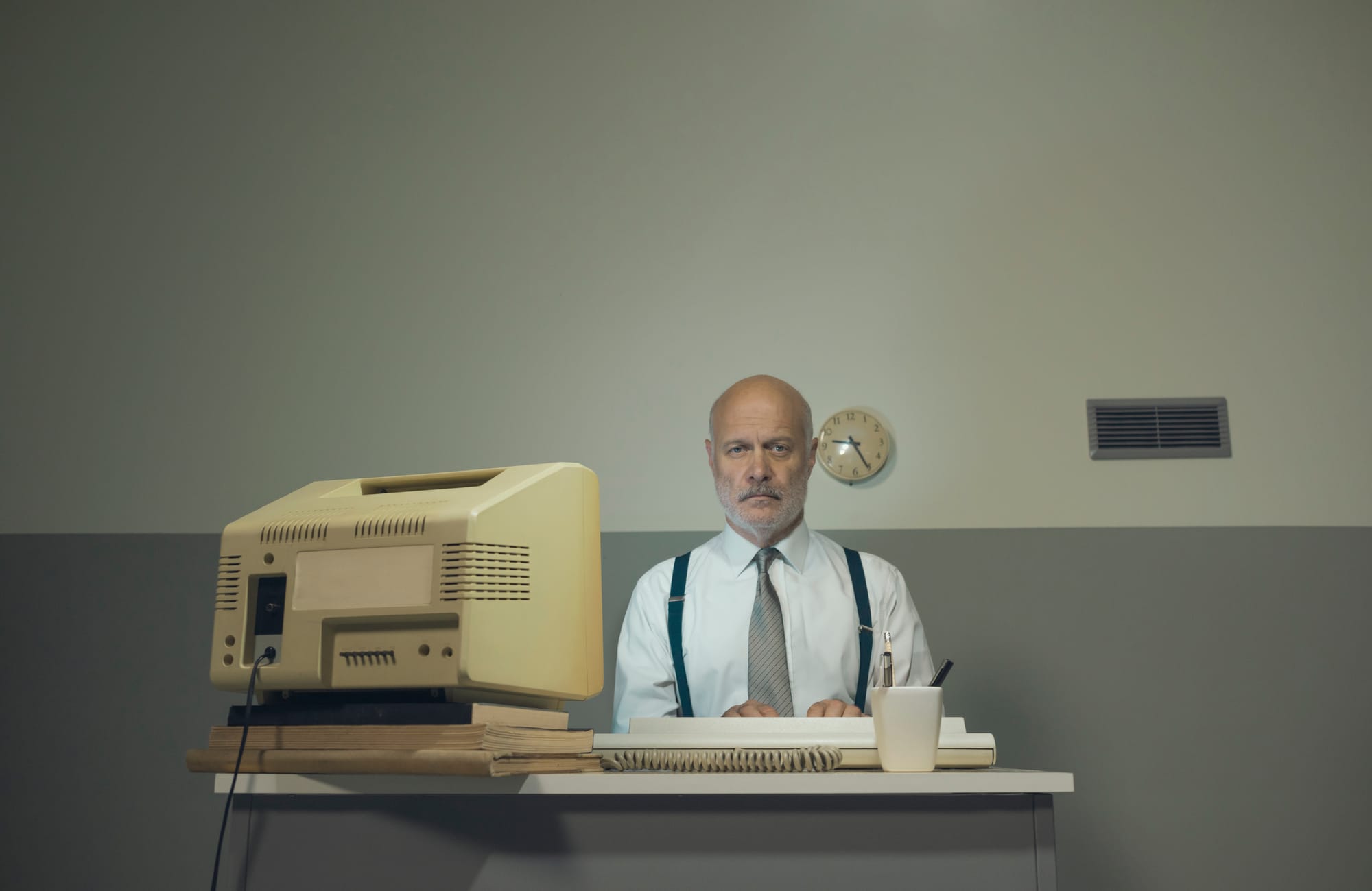 Une personne travaillant à un bureau et utilisant un écran et un clavier d'ordinateur d'époque. 