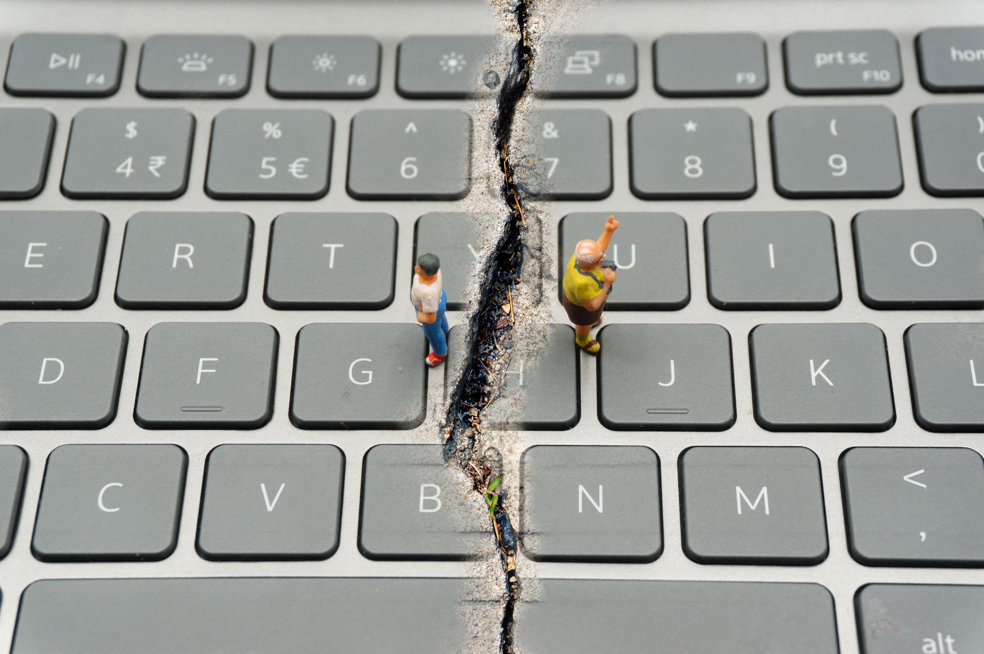 Two human figurines stand on a keyboard facing away from each other on either side of a crack. 