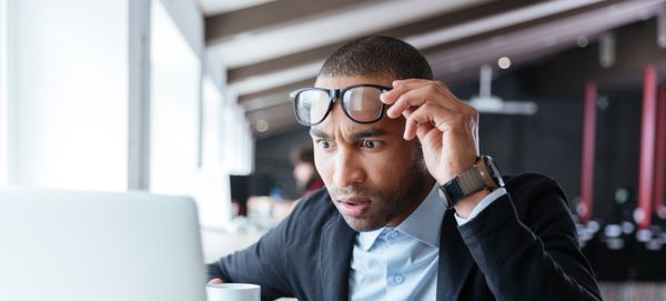 Une personne qui regarde un ordinateur portable en soulevant ses lunettes au-dessus de ses yeux, l’air préoccupé.