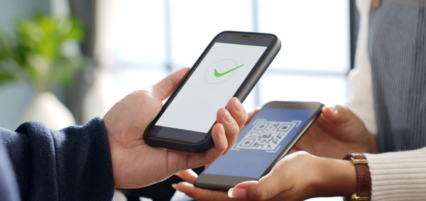 Person with a smartphone with a green check mark on their screen scanning a digital ID barcode on another smartphone.